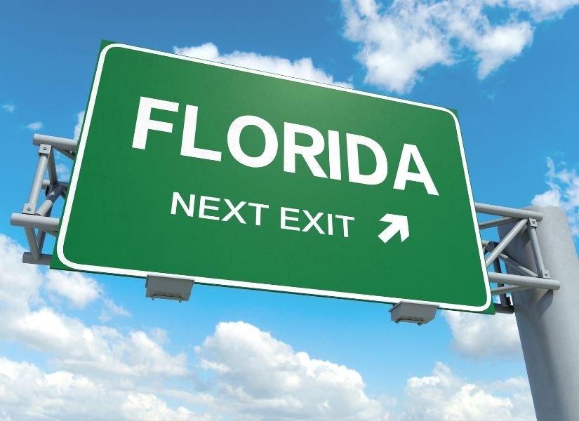 Green "Florida, Next Exit" sign against a blue sky with small white clouds