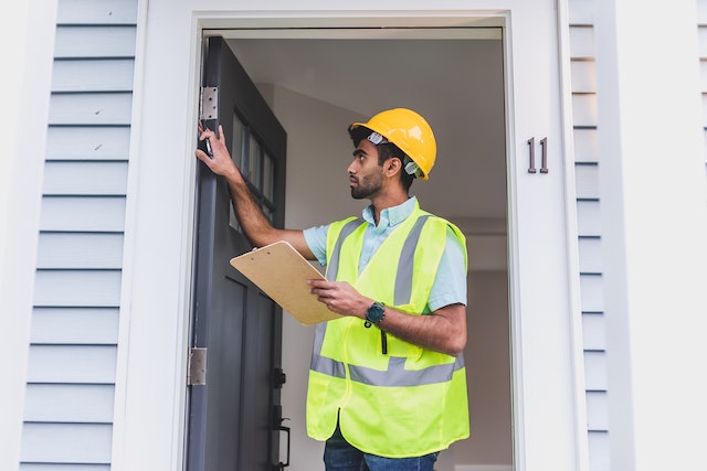 a-property-inspector-in-a-yellow-vest-and-hard-hat-looking-at-the-homes-doorway a-property-inspector-in-a-yellow-vest-and-hard-hat-looking-at-the-homes-doorway