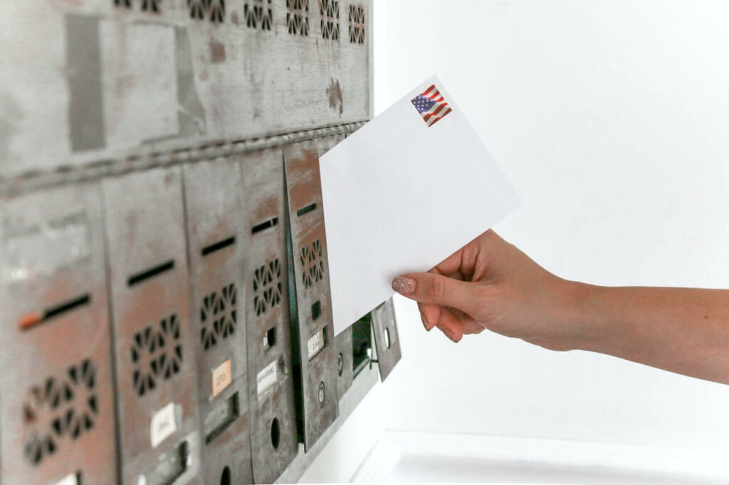 Hand slipping a white envelope into a silver mailbox