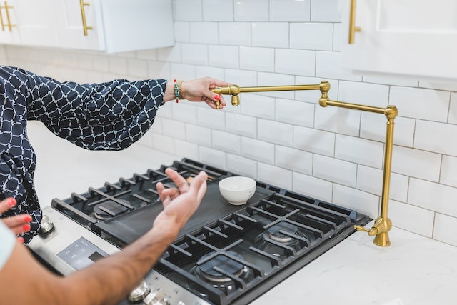 A hand holding a brass faucet tube over a stove